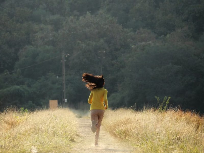 Young woman with long hair runs down a scenic path in summer. Embracing freedom and nature.
